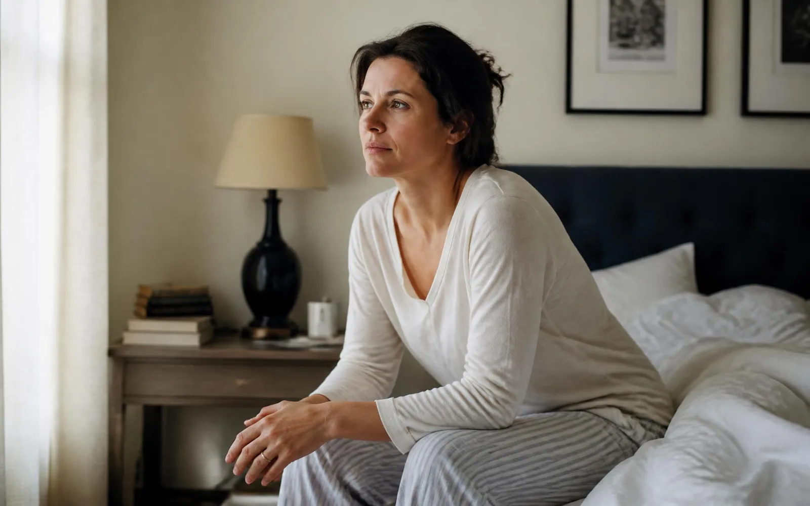 A woman in her forties sitting on the edge of her bed in soft morning light