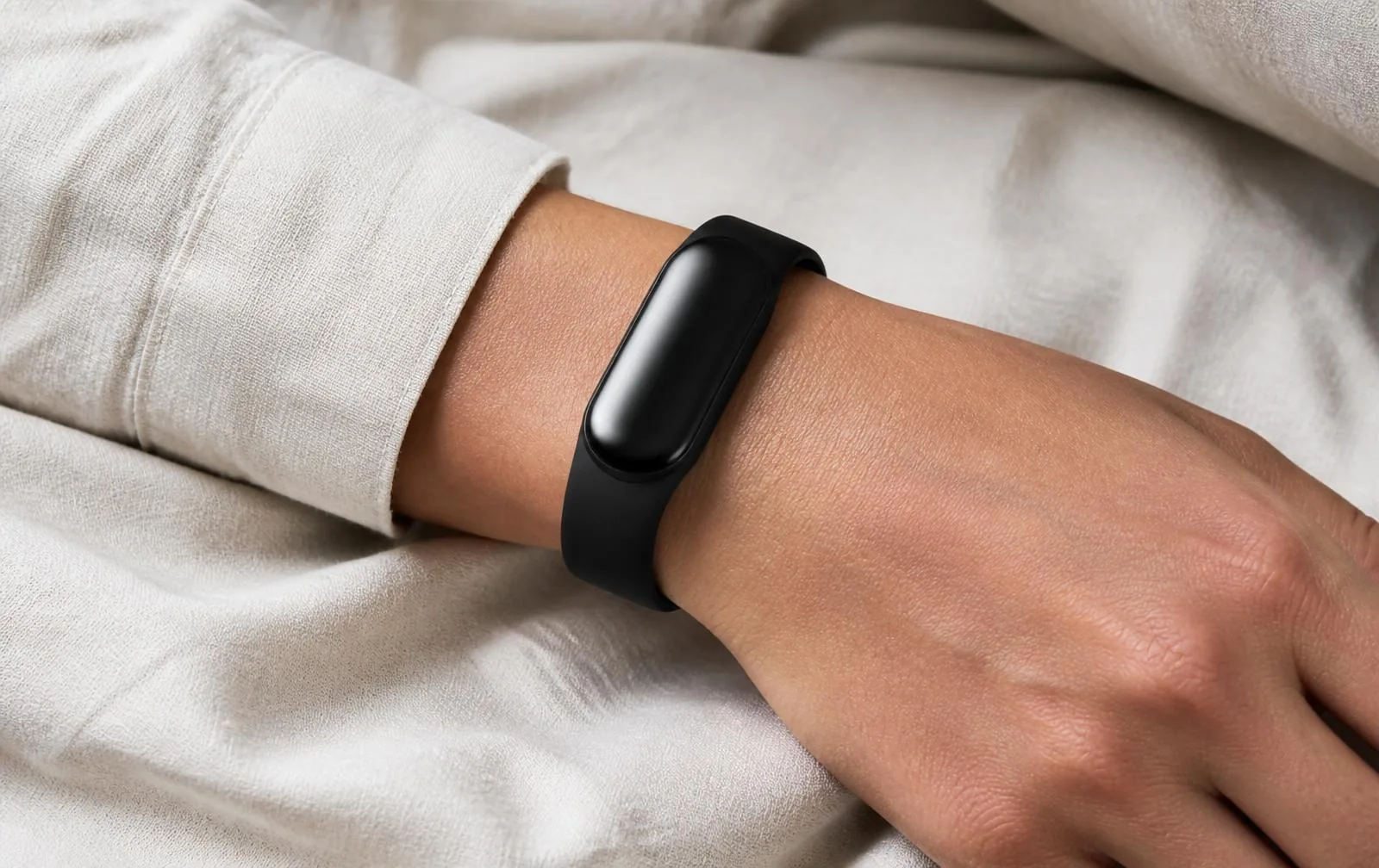 A sleep tracking band worn naturally on a wrist resting on linen
