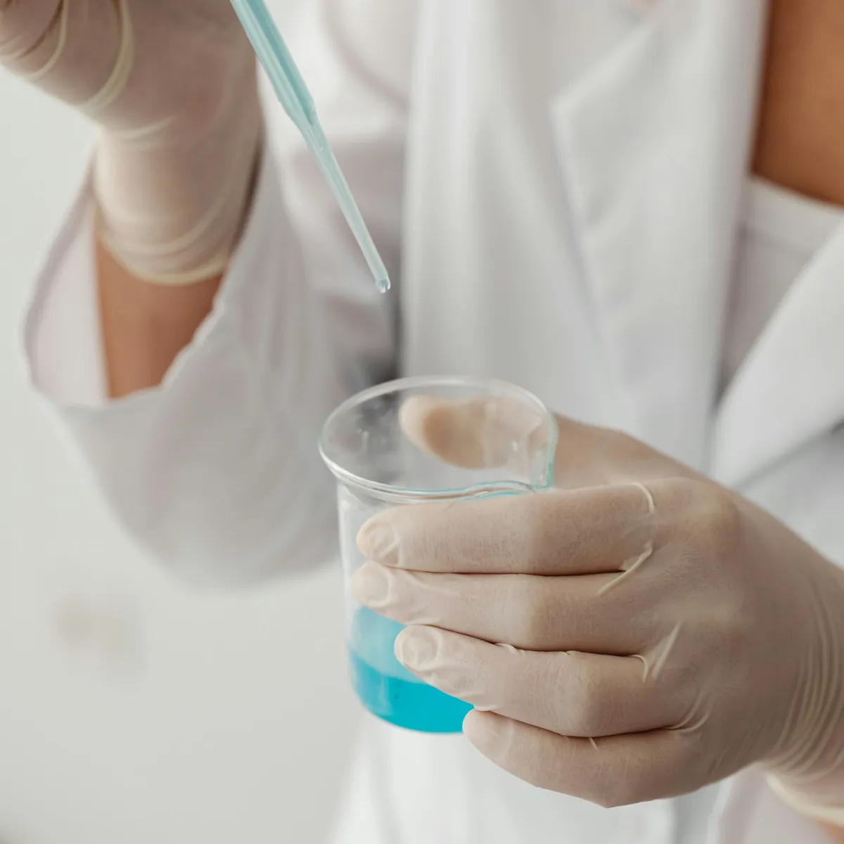 Gloved hands pipetting liquid into a laboratory beaker